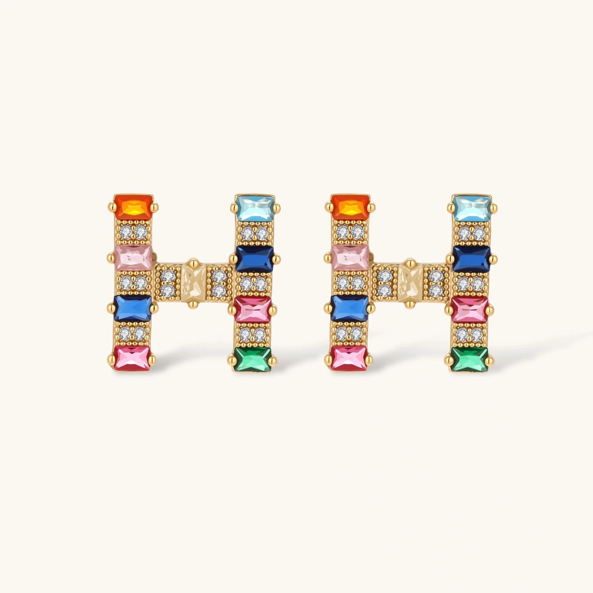 Gold-plated H initial pendant necklace and stud earrings set with multicolor baguette zirconia stones on cream background.